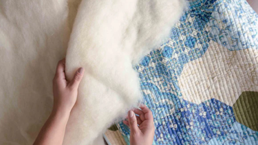 Hands using wool batting to finish a wool quilting project