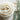 Close-up view of creamy white wool roving swirled in a soft spiral pattern beside fresh green herbs, showcasing the natural beauty and purity of premium American sustainable wool