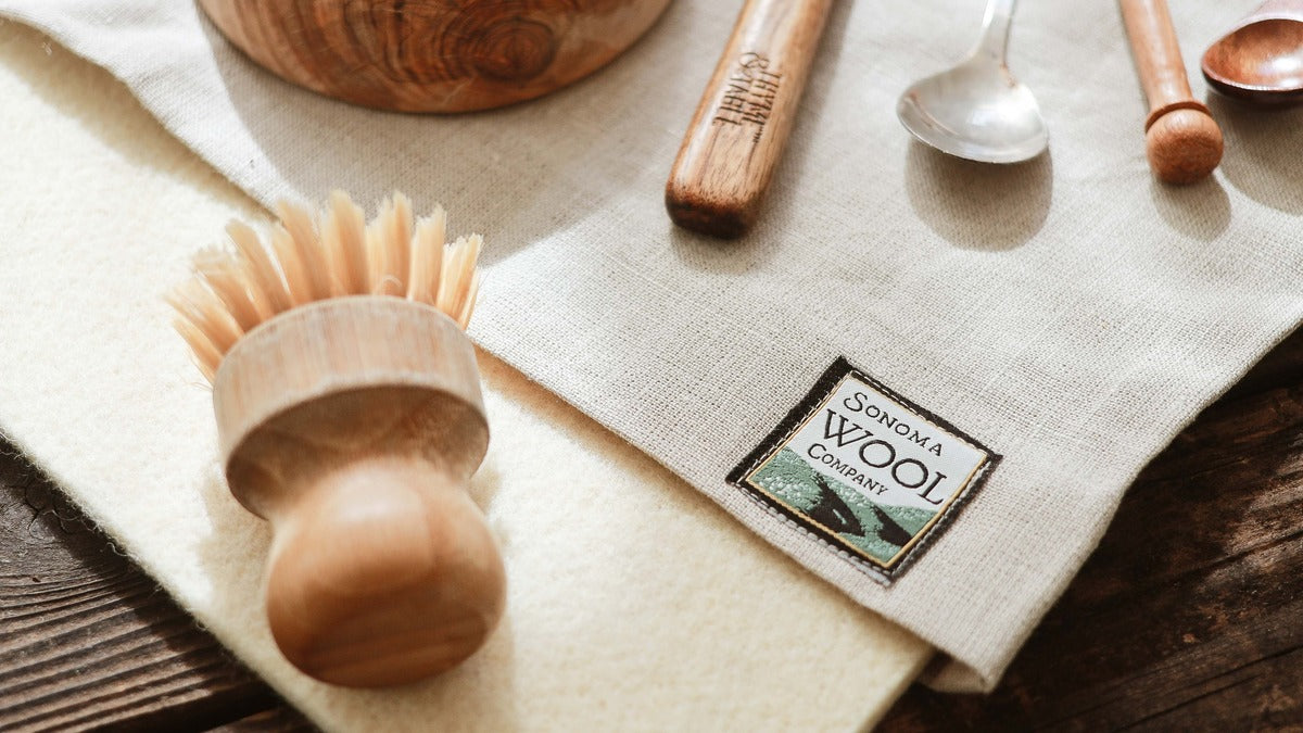 Brush with wooden handle sit on sustainable wool dish drying mat with natural linen sleeve by Sonoma Wool Company, featuring eco-friendly kitchen accessories and zero-waste cleaning tools