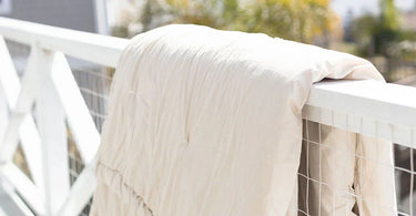 A wool blanket is drapped over the railing of a deck to dry in the sun instead of using a traditional dryer. 