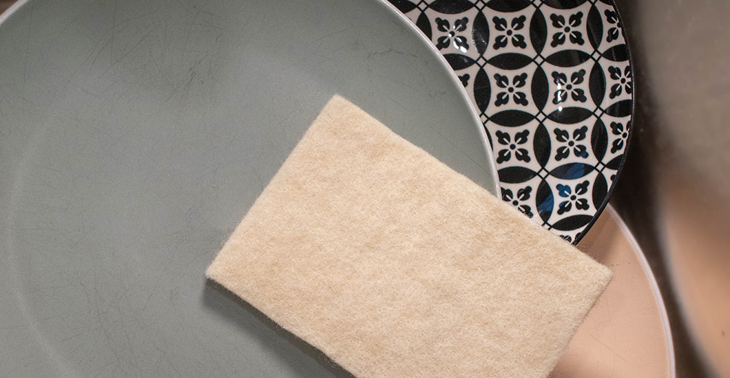 Eco-friendly 100% USA wool cleaning sponge displayed on artisanal ceramic plates - sustainable natural alternative to synthetic sponges that reduces environmental impact while providing superior cleaning performance for conscious homemakers