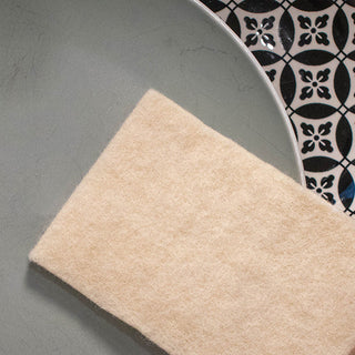 Eco-friendly 100% USA wool cleaning sponge displayed on artisanal ceramic plates - sustainable natural alternative to synthetic sponges that reduces environmental impact while providing superior cleaning performance for conscious homemakers