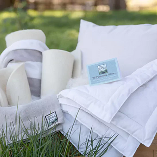 Premium wool bedding collection displayed on green grass showcasing sustainable luxury with crisp white duvet, pillow, and natural wool filling - eco-friendly home essentials for creating the ultimate cozy sanctuary in 2025