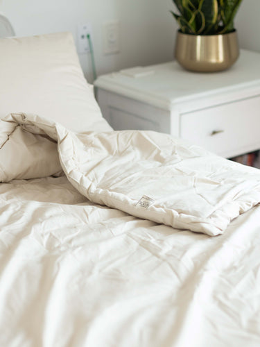 Plush white wool comforter with natural wrinkles against a light background, showcasing premium organic bedding that promotes healthy sleep with temperature-regulating merino wool