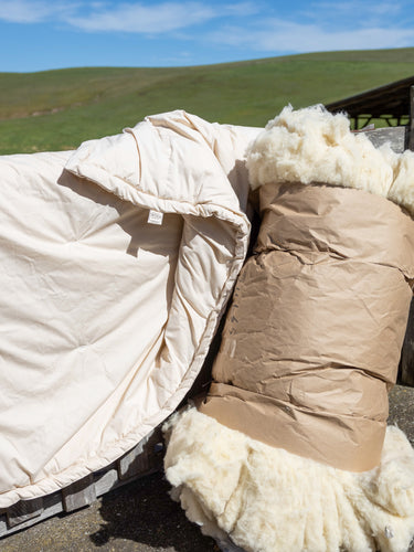 A Sonoma Wool Company Wool Comforter next to Wool Batting leaning up against a fence as part of their Wool Bedding Collection.