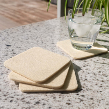 Three wool coasters stacked on a coffee table with a glass of water resting on a fourth coaster behind